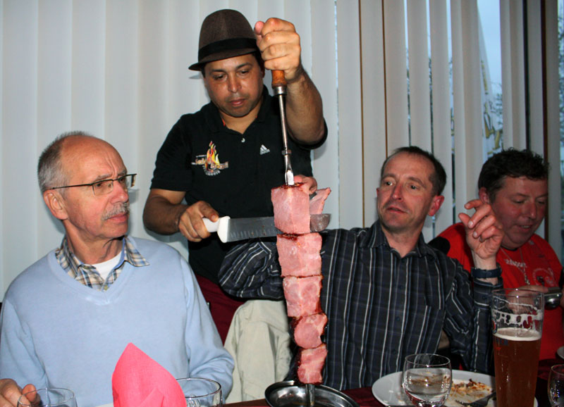 Rolf (links) und Manfred schauen genau hin wie Ratinho das Fleisch vom Spieß schneidet (Foto: Bettina Huber).