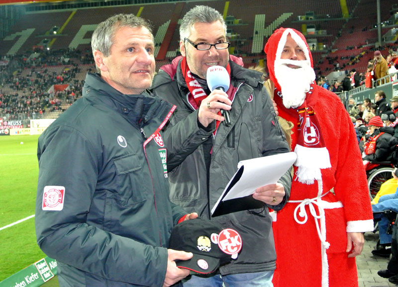  Stadionsprecher Horst Schömbs (mitte) informierte die Zuschauer auf den Rängen über das Geschehen vor der Südtribüne, während 1. FCK-Team-Manager Roger Lutz und der Nikolaus gespannt auf den Start der traditionellen „Weihnachts-Geschenk-Aktion“ warteten.